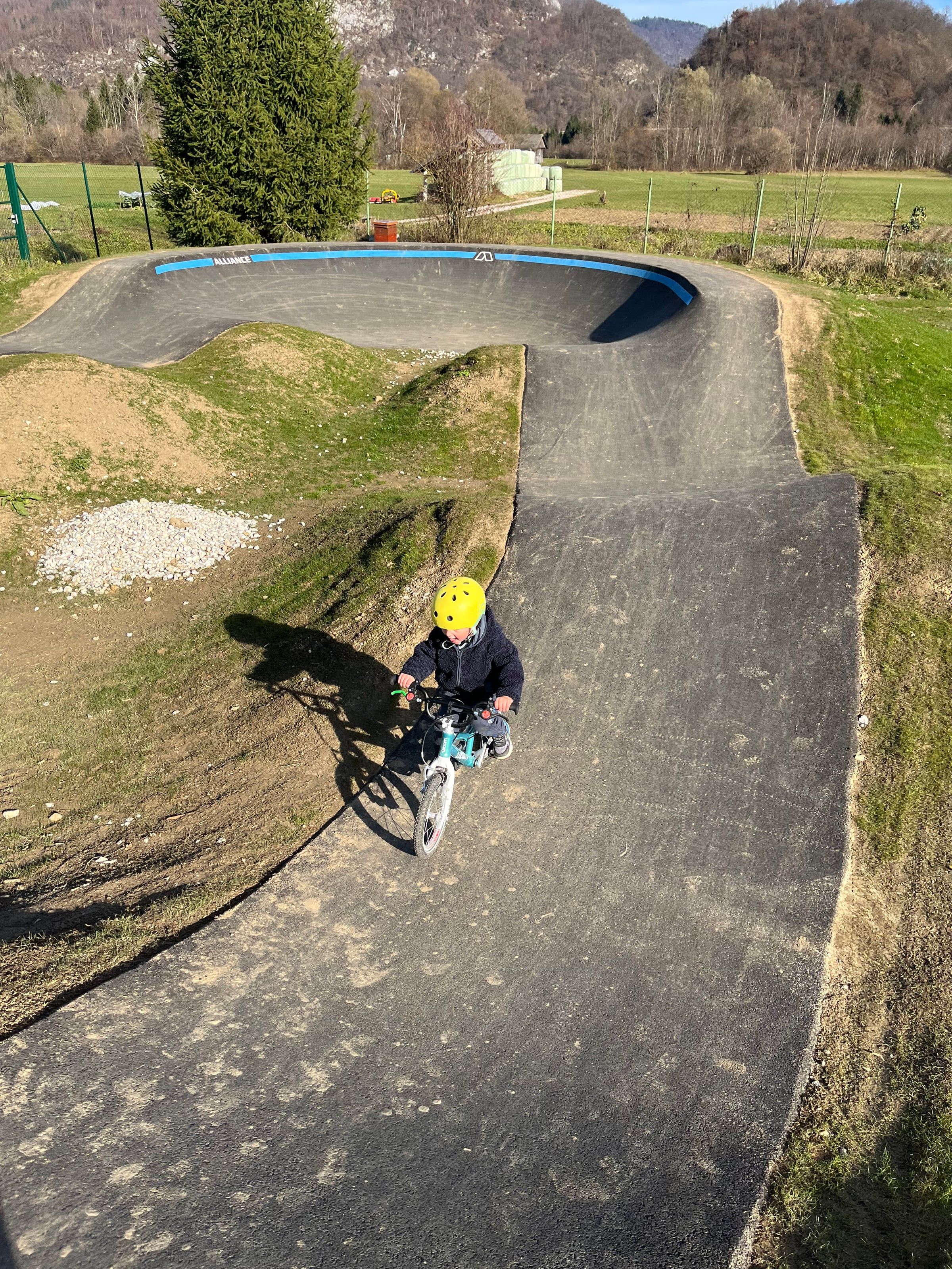 Otrok s čelado vozi kolo po asfaltnem pumptracku, posneto od zgoraj